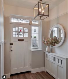 an entryway with a white door, mirror and vase filled with flowers on the table