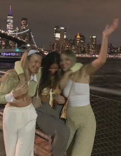 three women posing for the camera in front of a cityscape at night time