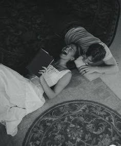 two people laying on the floor next to each other with a book in their hands