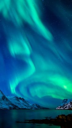 the northern lights shine brightly in the night sky over water and snow covered mountain tops