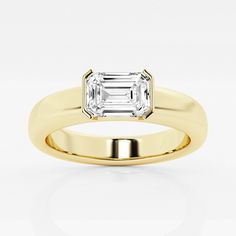 a yellow gold ring with an emerald cut diamond in the center, on a white background