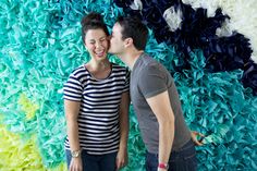 a man and woman standing next to each other in front of a wall covered with flowers