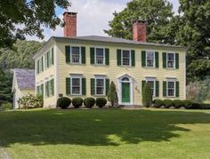 a large yellow house with green shutters on the front and side windows, surrounded by trees