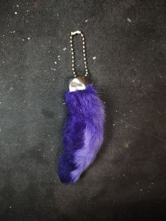 a purple furry animal keychain hanging from a metal ball chain on a black surface