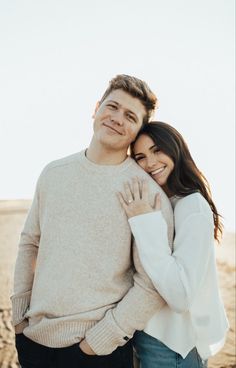 a man and woman standing next to each other in front of the ocean with their arms around each other