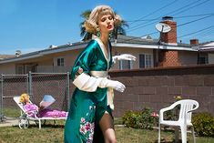 a woman in a green dress and white gloves is walking on the grass near a house