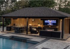 an outdoor living area next to a pool with a television on the wall and fireplace