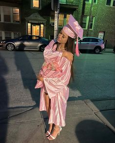 a woman in a pink dress and hat standing on the street