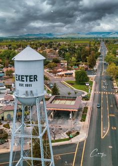 an aerial view of a street and water tower in the middle of town with storm clouds overhead