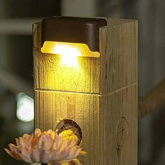 a light that is on top of a piece of wood with flowers in the background