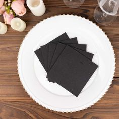 four black napkins sitting on top of a white plate next to candles and flowers