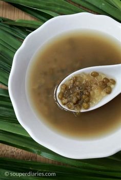 a spoon filled with soup sitting on top of a white bowl next to green leaves