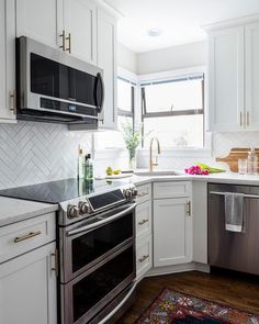 a kitchen with white cabinets, stainless steel appliances and an area rug on the floor