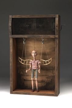 a doll in a wooden box with strings attached to the body and hands, standing on one leg