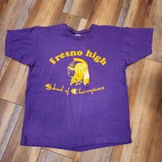 "Vintage single stitch Fresno high school, school of champions t shirt. Excellent used condition with minimal wear. Sized as a large fits more like a medium. Shirt is purple in color Measures: 21\" pit to pit 24\" shoulder to hem B02" Purple College T-shirt With Team Name, Purple School Spirit T-shirt With Graphic Print, 90s Purple T-shirt With Letter Print, 90s Style Purple T-shirt With Letter Print, Sports T-shirt Purple With Logo Print, Purple 90s Style T-shirt With Letter Print, Purple T-shirt With Team Name For Campus Wear, Purple Crew Neck T-shirt For School Spirit, Purple Short Sleeve T-shirt For School Spirit