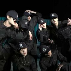 a group of young men in black outfits and hats posing for the camera with their arms around each other