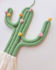 a green cactus with pink flowers and tassels hanging from it's side