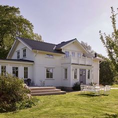 a large white house sitting on top of a lush green field next to a forest