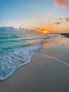 the sun is setting over the ocean with waves crashing on the beach and people walking in the water