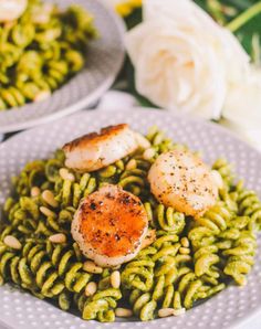 pasta with scallops and pesto sauce on a plate next to white roses