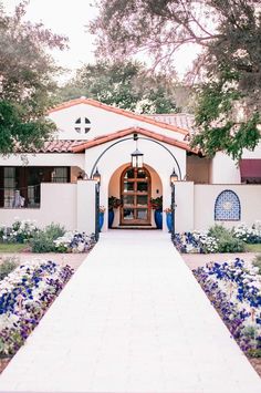 a white house with blue and purple flowers in the front yard