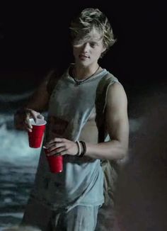 a young man holding a red cup in his right hand and standing next to the ocean