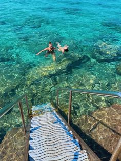 two people swimming in clear blue water next to some steps