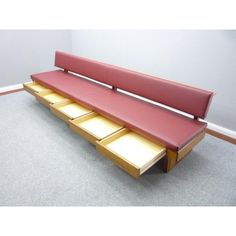 a red bench with drawers underneath it on the floor next to a wall in an empty room