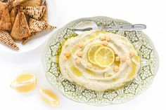 a plate filled with hummus and crackers next to a bowl of lemon wedges