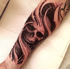 a man's arm with a skull and flames tattoo design on the left forearm