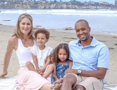 a man and two women sit on the beach with their children in front of them