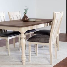 a dining room table with two chairs and a vase on top of it, in front of a white rug