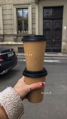 a woman holding up a cup of coffee in front of a building with the words monday written on it