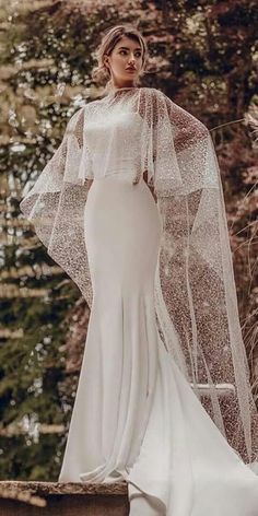 a woman wearing a wedding dress and veil standing in front of some trees with her hands on her hips