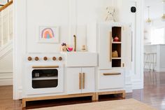 a white play kitchen with an oven, sink and stairs leading up to the second floor