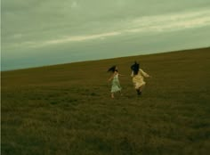 two girls running in a field with one holding the other's hand