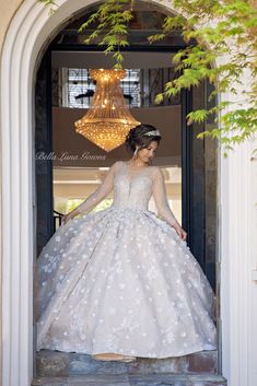 a woman in a wedding dress is standing on the steps to an open door with a chandelier hanging above her