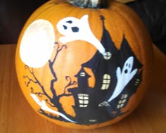 an orange pumpkin decorated with black and white ghost houses on it's side, sitting on a wooden table