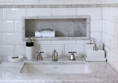 a bathroom with marble counter tops and white tiles on the walls, along with soap dispensers