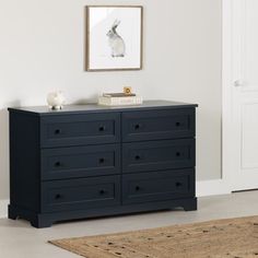 a black dresser in a white room with a rug on the floor and pictures above it