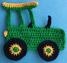 a crocheted green and black toy truck on a blue surface with yellow accents