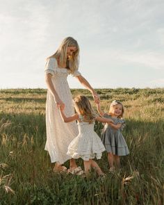 a woman and two children are standing in tall grass together, both holding their hands