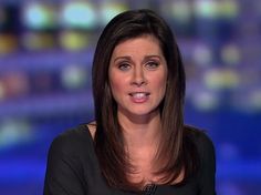 a woman with long hair sitting down in front of a news desk and looking at the camera