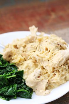 a white plate topped with chicken and spinach covered in gravy on top of a wooden table