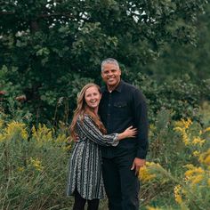 an older man and young woman posing for a photo in front of some wildflowers