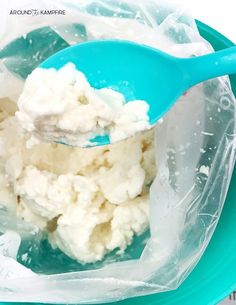 a plastic container filled with ice cream on top of a blue plate next to a spoon