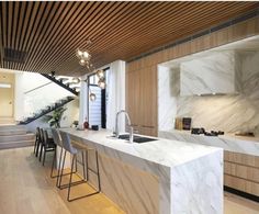 a modern kitchen with marble counter tops and wooden cabinets, along with stairs leading up to the second floor