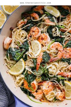 shrimp and spinach pasta in a pan with lemon wedges