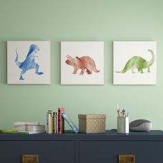 three dinosaur paintings hang on the wall above a dresser in a child's room