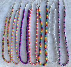 several different colored beads are on a white surface and one is hanging from a silver chain